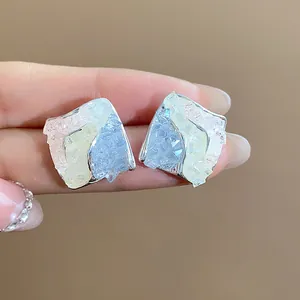 Primo piano di orecchini a lobo romboidali in argento con vetro colorato frantumato.