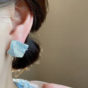 Dettaglio di un orecchino a perno argentato con trama artistica effetto ghiaccio.