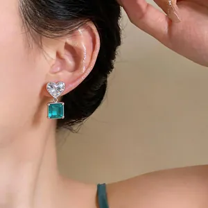 Close-up detail of silver heart stud with emerald square zircon drop earrings on ear
