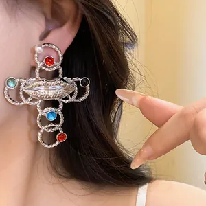 A detailed macro view of a vintage silver cross earring featuring pearl and lip accents