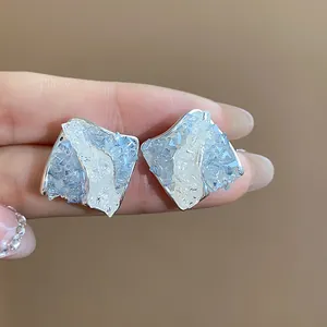 Dettaglio di orecchini a lobo in argento a forma di rombo con texture cristallina blu e bianca.