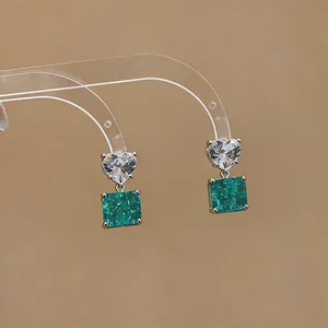Macro detail showing heart-shaped zircon and square emerald green silver earrings