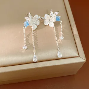 Dettaglio di orecchini a fiore in zircone con nappe e accenti blu su scatola dorata.