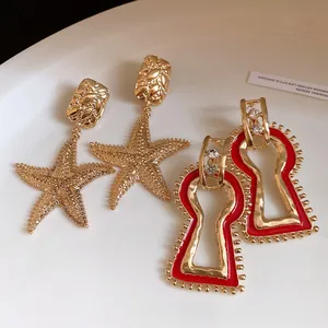 Macro view of vintage gold starfish earrings and red enamel keyhole drop earrings on white plate