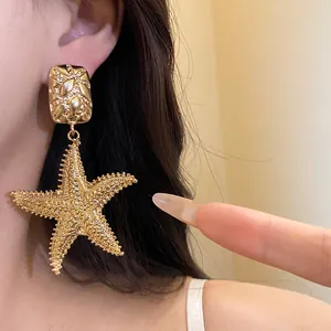 Macro view of vintage gold starfish drop earrings worn on ear showing intricate texture detail