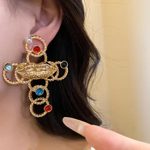 Detailed close-up of a vintage golden cross earring with lip motif and colorful stones.