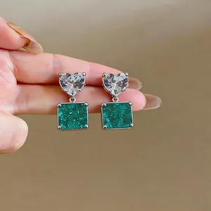 Close-up detail of silver needle earrings with heart zircon and square green stones