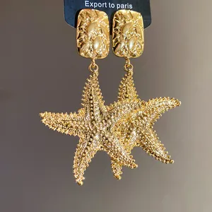 Close-up of vintage gold textured starfish dangle earrings on a black display card