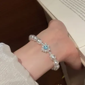 Detailansicht eines Vintage-Perlenarmbands mit blauem Herz-Edelstein am Handgelenk.