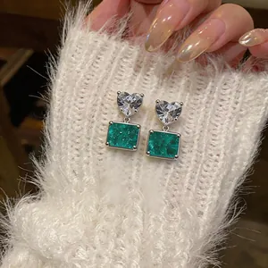 Macro detail of heart-shaped zircon and emerald green square drop earrings on white knit
