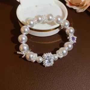 Detailansicht eines eleganten Perlenarmbands mit Kristallherz- und silbernen Schleifenanhängern.