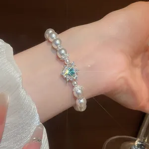 Detailansicht eines eleganten Perlenarmbands mit funkelndem blauem Herz-Edelsteinanhänger.