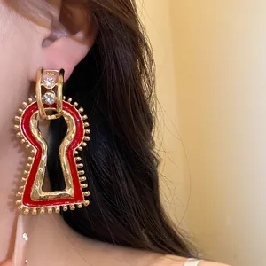 Close-up of retro keyhole pendant earring with red enamel and gold finish