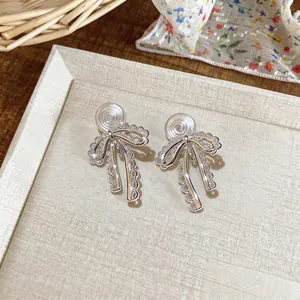 Close-up of silver bow clip-on earrings with delicate lace hollow design.