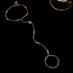 Detailed view of a gold-toned star and zircon hand chain slave bracelet with ring.