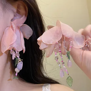 Vue détaillée des boucles d'oreilles fleurs en tissu rose avec des accents de perles colorées.