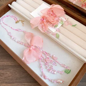 Gros plan d'un collier à pampilles en perles roses avec fleurs en tissu et feuilles vertes