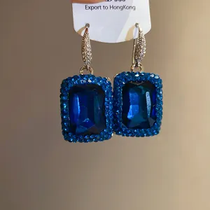 Detailaufnahme von eleganten quadratischen blauen Edelstein-Ohrringen mit Strass-Halo