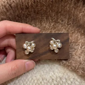 Detailed view of elegant pearl stud earrings featuring a zircon ribbon design on wood
