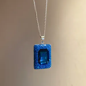 Nahaufnahme eines blau funkelnden quadratischen Edelsteinanhängers mit Kristallrand