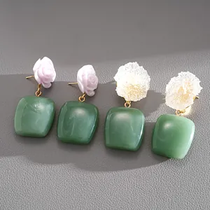 Detalle de pendientes de flores de resina con cuadrados verdes en rosa y blanco