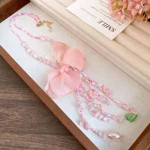 Vue détaillée d'un collier de perles rose avec fleur en tissu et pompons élégants.