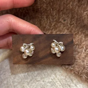 Close-up of elegant pearl stud earrings with zircon bow design on a wooden display.