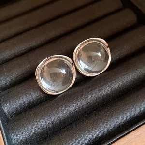 Macro view of transparent round resin stud earrings with organic silver metal frame on tray.