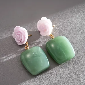 Primer plano de pendientes de flores de resina con rosas rosas y cuadrados verdes en cuero