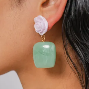 Primer plano de pendientes colgantes de resina con diseño de rosa y cuadrado en oreja
