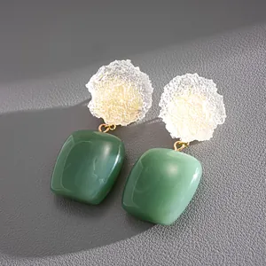 Primer plano detallado de pendientes cuadrados de resina con textura verde y blanca.
