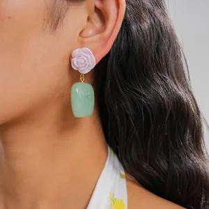 Detalle de pendientes de flor violeta y gota verde usados por una modelo en primer plano