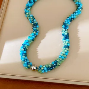 Vue détaillée d'un collier en perles de verre tressées bleues et vertes, fermoir aimanté.