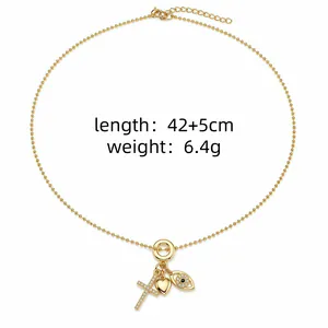 Détail du collier plaqué or avec des pendentifs en forme de croix, de cœur et d'œil.