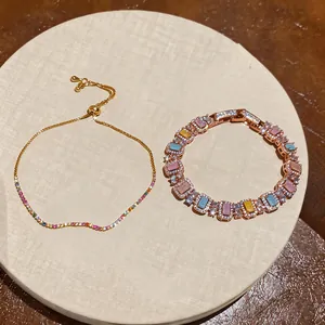 Close-up of shiny zircon bracelets with colorful square stones and delicate gold chain.