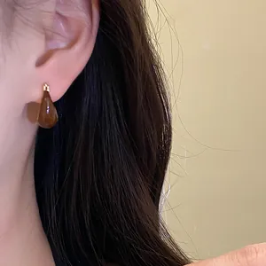 Close-up detail shot of elegant brown resin teardrop earrings worn on a model's ear