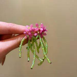 Macro view of handmade pink beaded flower earrings featuring fresh green tassel details