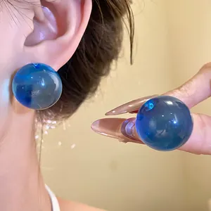 Primo piano di orecchini a lobo minimalisti in resina blu a forma di sfera lucida.