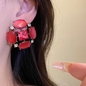 Dettaglio di orecchini vintage con pietre occhio di gatto rosse e strass luccicanti.