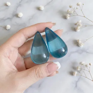 Eleganti orecchini a perno a goccia in resina blu traslucida su sfondo di marmo bianco chic