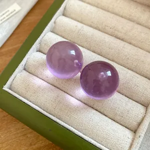 Primo piano di eleganti orecchini a lobo sferici in resina viola in una scatola portagioie verde