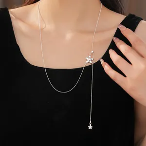 Close-up of a minimalist silver flower lariat necklace worn against a sleek black dress.
