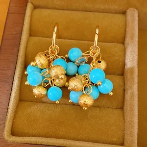 Close-up detail of 18k gold-plated cluster earrings with blue and gold beads in box