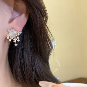 Detailed view of sparkling star stud earrings with dangling crystals worn on the ear.
