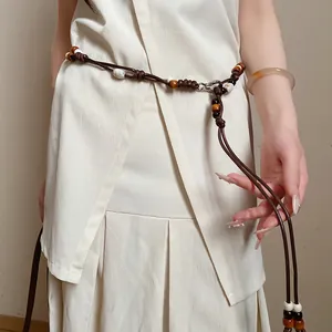 Close-up of ethnic braided leather waist chain with wooden beads on a cream dress.