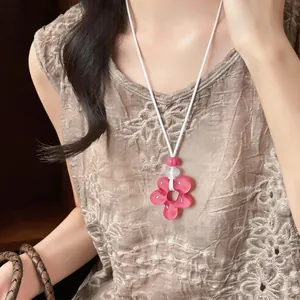 Détail d'un collier avec pendentif fleur en résine rose sur cordon blanc porté par un mannequin