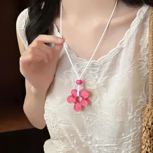 Détail d'un collier pendentif fleur en résine rose avec cordon en cuir blanc sur un modèle