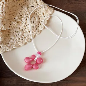 Vue détaillée d'un collier pendentif fleur en résine rose avec cordon en cuir blanc