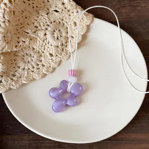 Gros plan d'un collier pendentif fleur en résine violette sur une assiette blanche.