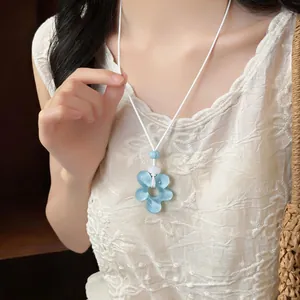 Gros plan d'un collier avec pendentif fleur en résine bleue sur un cordon blanc